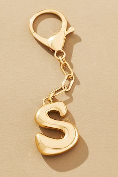 a gold key chain with the letter s hanging from it's end, on a beige surface