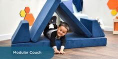 a young boy laying on the ground in front of a large blue structure with he's smiling