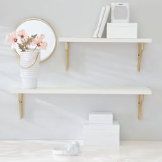 a white shelf with flowers and books on it next to a computer mouse, headphones and a mirror