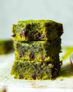 three pieces of green cake stacked on top of each other next to a small bowl