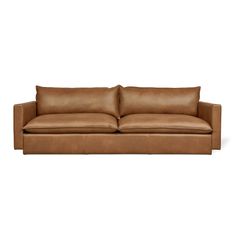 a brown leather couch with two pillows on it's back and one arm facing the camera