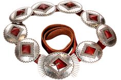 an assortment of silver and red jewelry on a wooden table with a brown leather belt