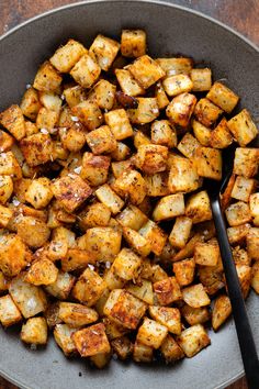 a plate full of cooked potatoes with a spoon in it and some seasoning on the side