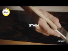 a person is holding a paintbrush and painting the word stain on a wooden surface