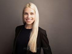 a woman with long blonde hair smiling at the camera while standing in front of a gray background