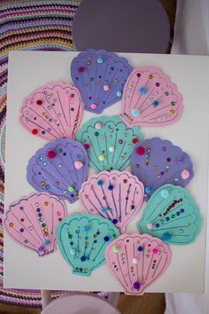 there are many different types of seashells on the white tablecloth with pink, blue and purple colors