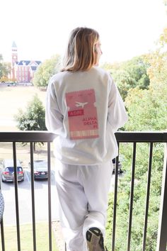 a woman standing on top of a balcony next to a railing wearing white sweatpants