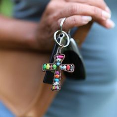 a person holding a cross shaped keychain with beads on it's side