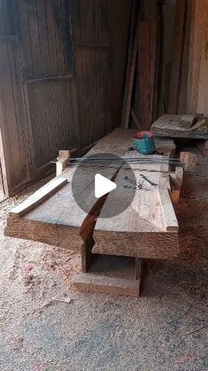 a wooden bench sitting in the middle of a dirt floor next to a building with wood planks on it