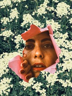 a woman's face is seen through a hole in the middle of some flowers