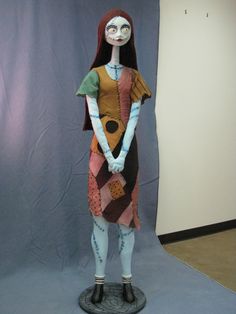 a doll is dressed up as a woman with long hair and makeup, standing in front of a gray backdrop