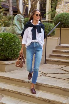 a woman walking down some steps carrying a purse and wearing jeans, a white shirt and black scarf