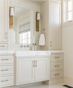 a bathroom with white cabinets and marble counter tops, along with a large mirror on the wall