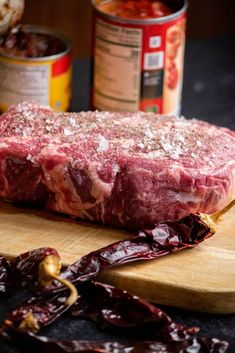 raw meat sitting on top of a wooden cutting board next to some chili sauces