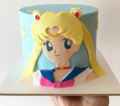 a hand holding up a cake with a sailor girl on it's face and ears