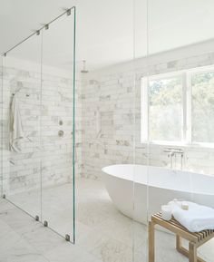 a white bathtub sitting next to a window in a bathroom with marble walls and floors