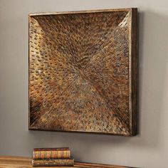 a wooden table topped with books and a metal art piece on the wall above it