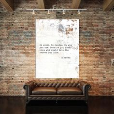 a brown leather couch sitting in front of a brick wall with a quote on it