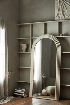 a large white mirror sitting on top of a wooden floor next to a book shelf