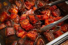 the meat is being cooked in the pan with tongs and sauce on it's side