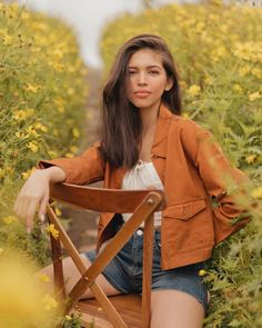 a woman sitting on a chair in the middle of a field with yellow wildflowers