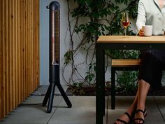 a woman sitting at a table with a glass of wine in front of an electric heater