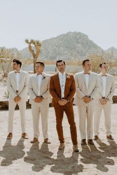 a group of men standing next to each other wearing suits and bow ties in the desert