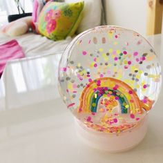 a glass ball with sprinkles and a rainbow in it on a table