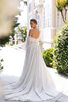 a woman in a white wedding dress standing on the sidewalk with her back to the camera