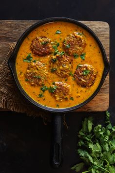 a pan filled with food sitting on top of a wooden cutting board next to some parsley