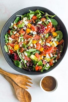 a salad in a bowl next to a wooden spoon on a white counter top with a wooden serving utensil