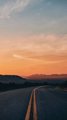 the sun is setting on an empty road with mountains in the distance and blue skies