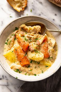 a white bowl filled with chicken and vegetable soup on top of a marble countertop