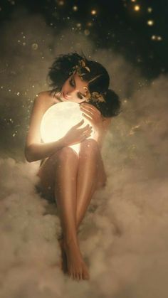 a woman sitting in the clouds holding a white ball with lights shining on her chest