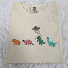 a white t - shirt with three dinosaurs and an alien flying in the sky