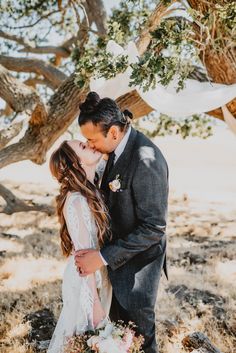 a bride and groom kissing under a tree