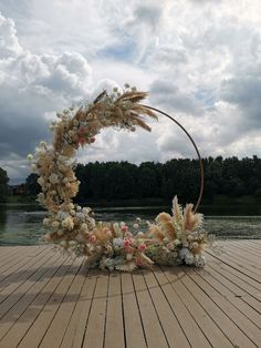 a wooden floor topped with a circular wreath filled with lots of flowers and plants next to a body of water