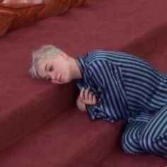 a young boy laying on top of a red carpeted floor next to a bed