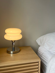 a lamp is sitting on top of a dresser next to a bed with white sheets