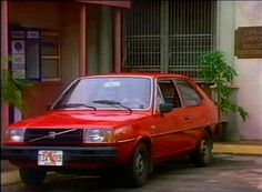 an old red car parked in front of a building next to a potted plant