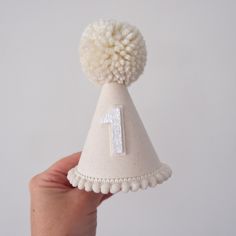 a hand holding a small white party hat with the number one on it's side