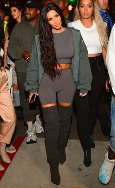 the two women are walking together in tight pants and crop tops, one is wearing black boots