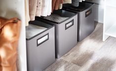 three bins with clothes hanging on them in front of a white cabinet and wooden floor