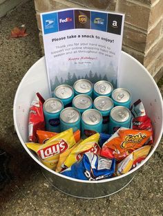 a bucket filled with lots of different types of drinks and snacks next to a sign that says, please take a snack to enjoy