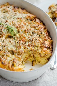 a casserole with cheese and herbs in a white dish next to a spoon