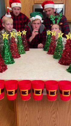 a group of people sitting around a table with christmas decorations on it and cups in front of them