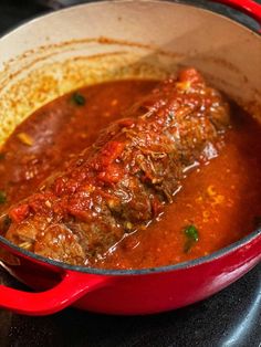 a red pot filled with meat covered in gravy on top of a stove