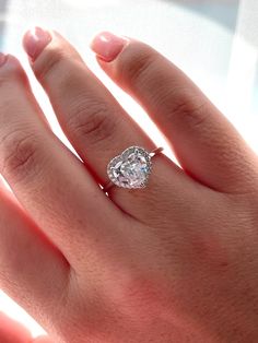 a woman's hand with a diamond ring on top of her finger and the other hand holding an engagement ring