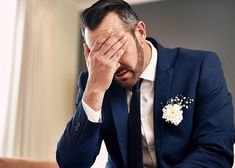 a man in a suit is holding his hand to his face as he sits on a couch