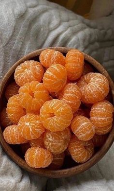 a wooden bowl filled with oranges on top of a bed